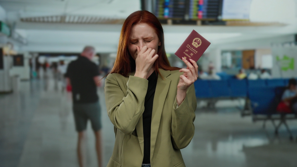 Woman,Holding,Chinese,Passport,Covers,Nose,In,Busy,Airport,Terminal,